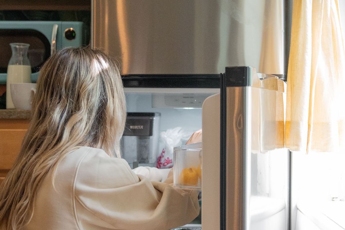 A woman choosing food from an open refrigerator